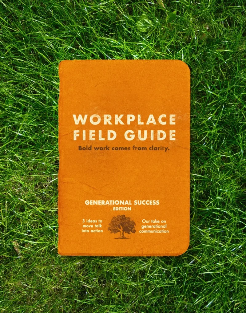 Orange booklet titled “Workplace Field Guide” lying on green grass. The cover reads “Bold work comes from clarity” and “Generational Success Edition,” with smaller text about moving talk into action and generational communication alongside a tree illustration.