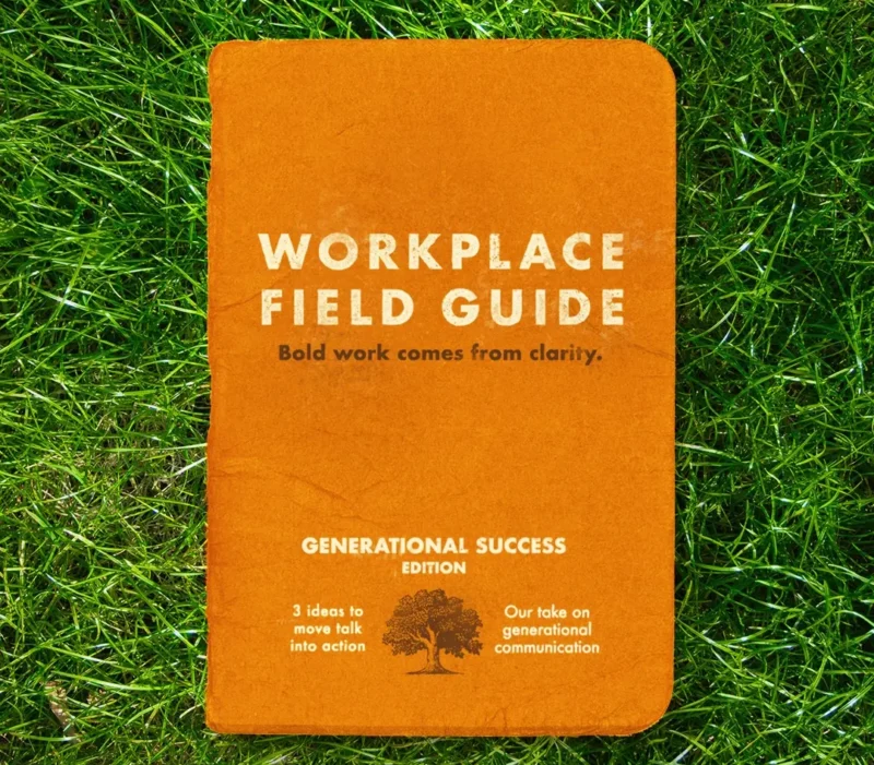 Orange booklet titled “Workplace Field Guide” lying on green grass. The cover reads “Bold work comes from clarity” and “Generational Success Edition,” with smaller text about moving talk into action and generational communication alongside a tree illustration.